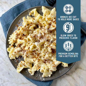 Prepared Sfoglini Trumpets pasta with cheesy white sauce on a dish. With product feature icons and text - Bronze die cut to hold more sauce. Slow dried to preserve flavor. Premium semolina for a better bite.