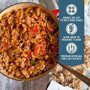 Prepared Sfoglini Whole Grain Reginetti pasta with peppers and sausage and red sauce in a pot. With product feature icons and text - Bronze die cut to hold more sauce. Slow dried to preserve flavor. Premium semolina for a better bite.