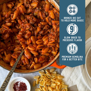 Prepared Sfoglini Saffron Malloreddus pasta with red meat sauce in a pot. With product feature icons and text - Bronze die cut to hold more sauce. Slow dried to preserve flavor. Premium semolina for a better bite.