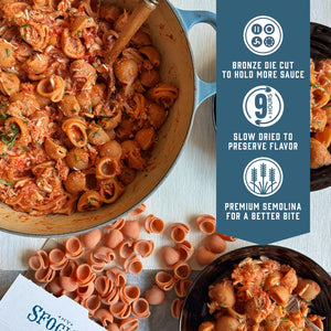Prepared Calabrian chili lumache pasta with crab sauce in a pot with plates. With product feature icons and text - Bronze die cut to hold more sauce. Slow dried to preserve flavor. Premium semolina for a better bite.