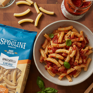Prepared Sfoglini Classic Italian Pantry Set  featuring Spacatelli  pasta in a bowl with a jar of sauce and Sfoglini pasta packaging on a wooden surface.